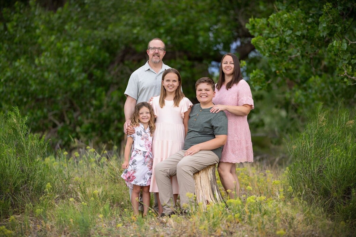 family of five with two girls and a boy sitting on a log in a wooded area