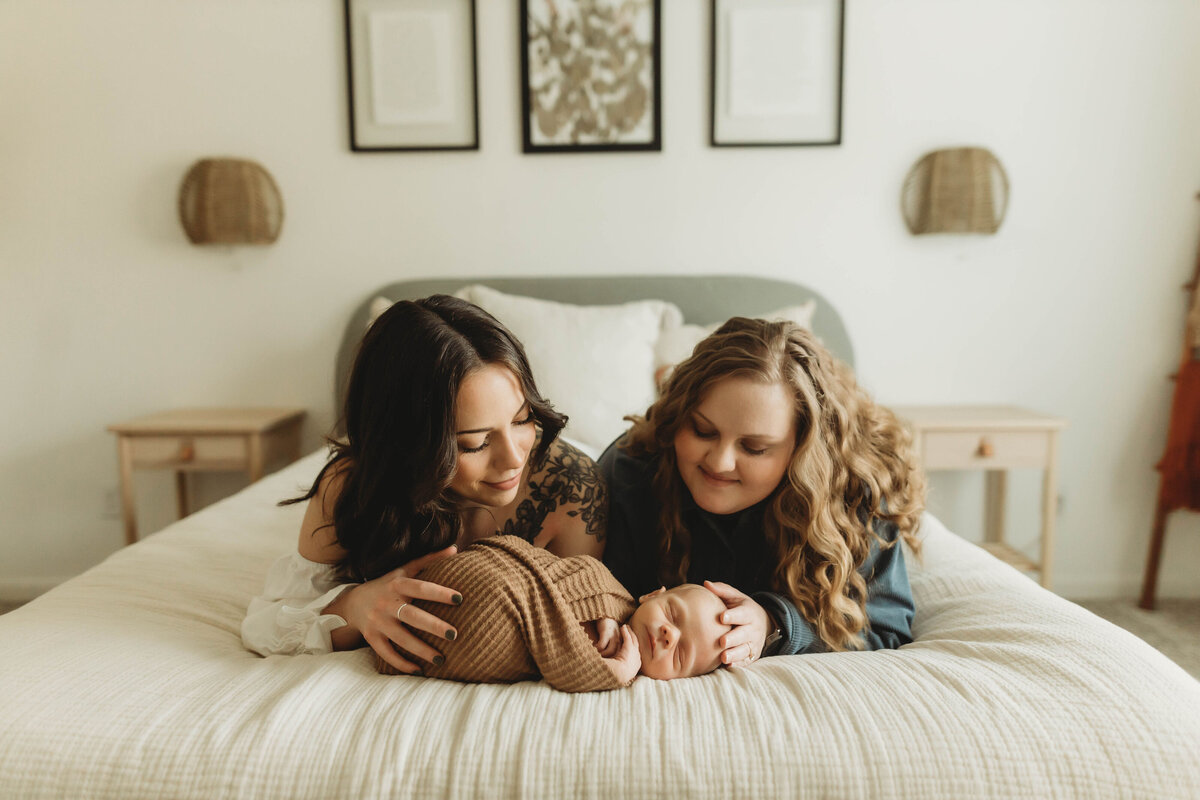 Two mothers laying on a bed with their newborn baby.