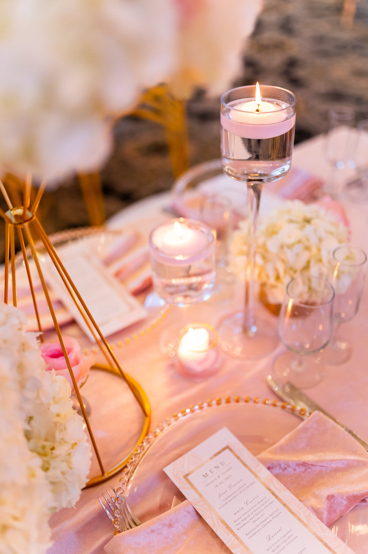 table decorated with a pink cloth, glass plates with gold accents, and glass candle holders