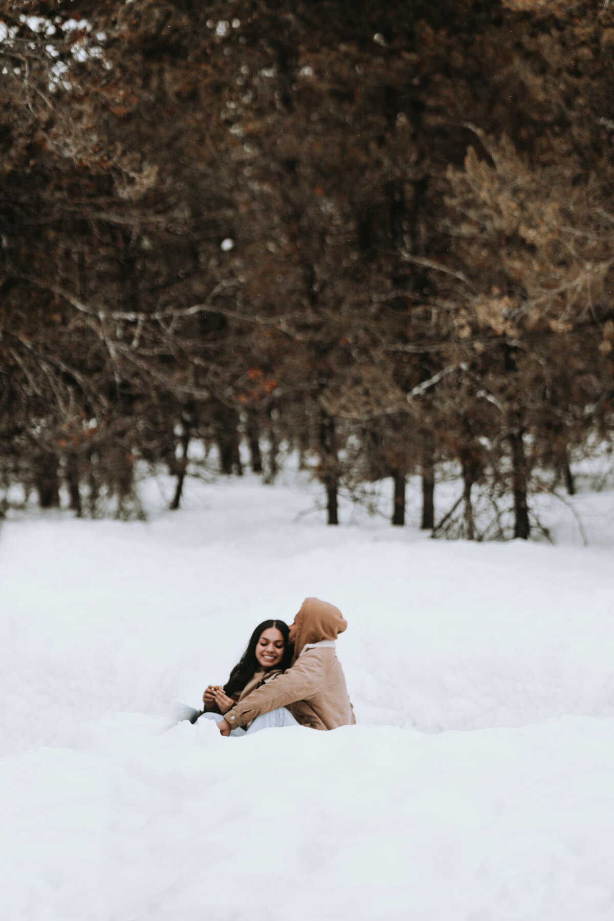 Engaged couple are encompassed by snow while keeping each other smiling and warm captured by Idaho Falls Couple Photographer
