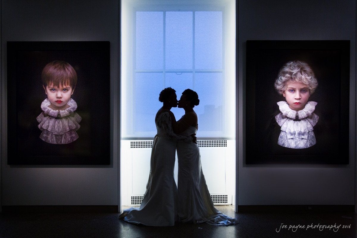 Two brides kissing in a darkly lit museum .