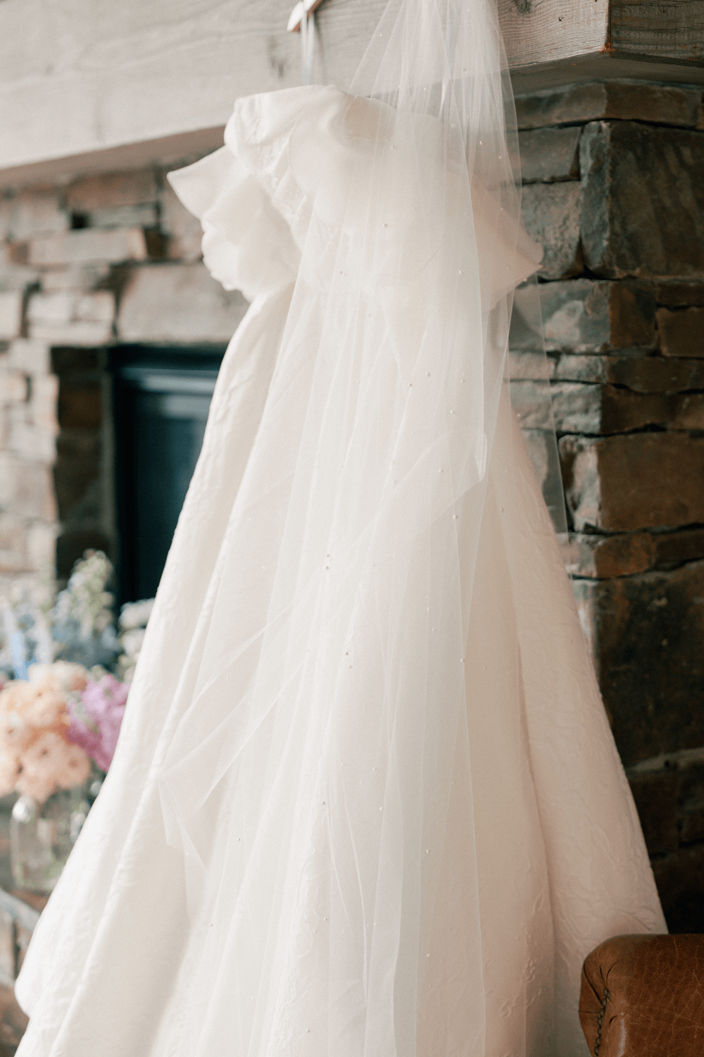 Bride’s wedding dress and veil hanging by a stone fireplace before a pastel summer wedding at Moonlight Basin.