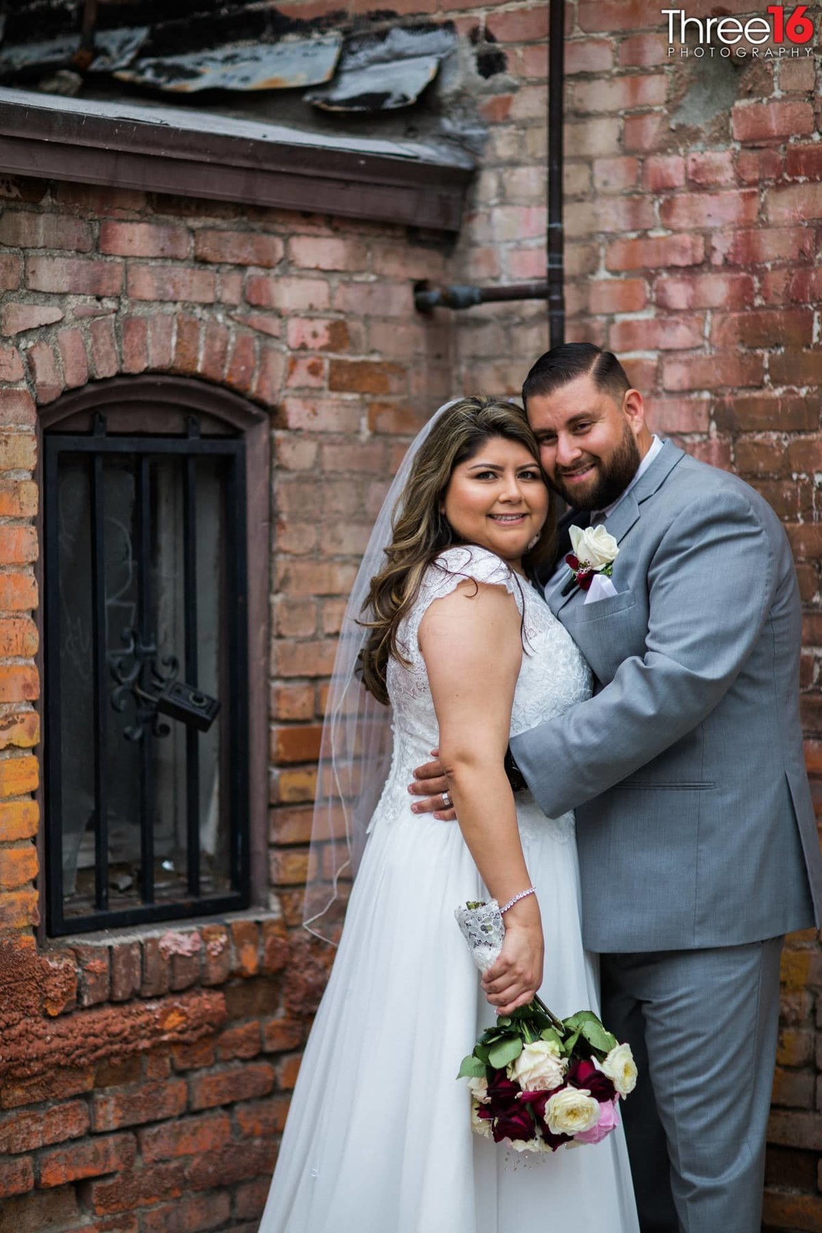Gentle embrace between Bride and Groom in back ally of Downtown Orange with brick walls behind them