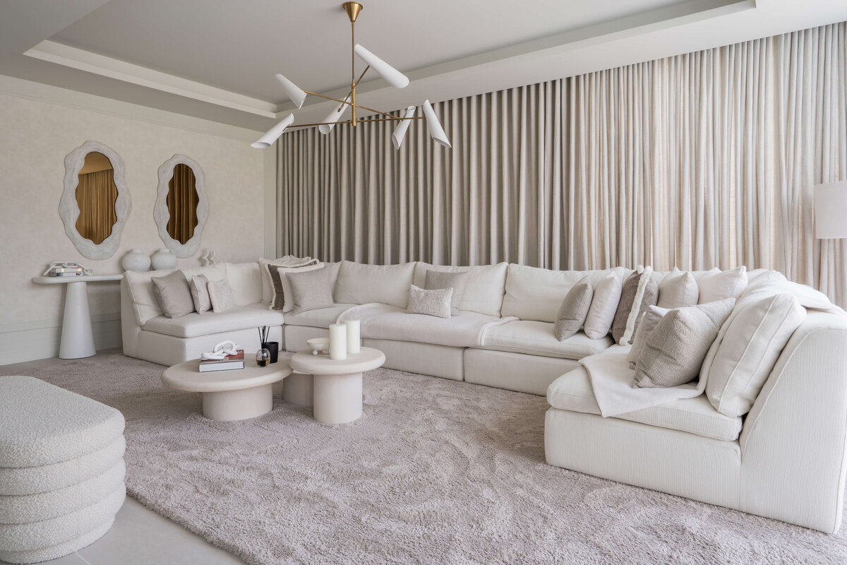 Spacious, modern living area with a large white sectional and white center table. Behind the couch is a white console table and two contemporary white mirrors.