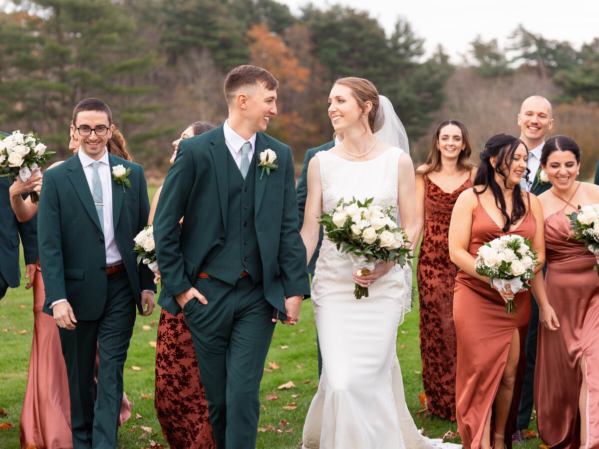 Bride and groom smile as they walk with their wedding party.