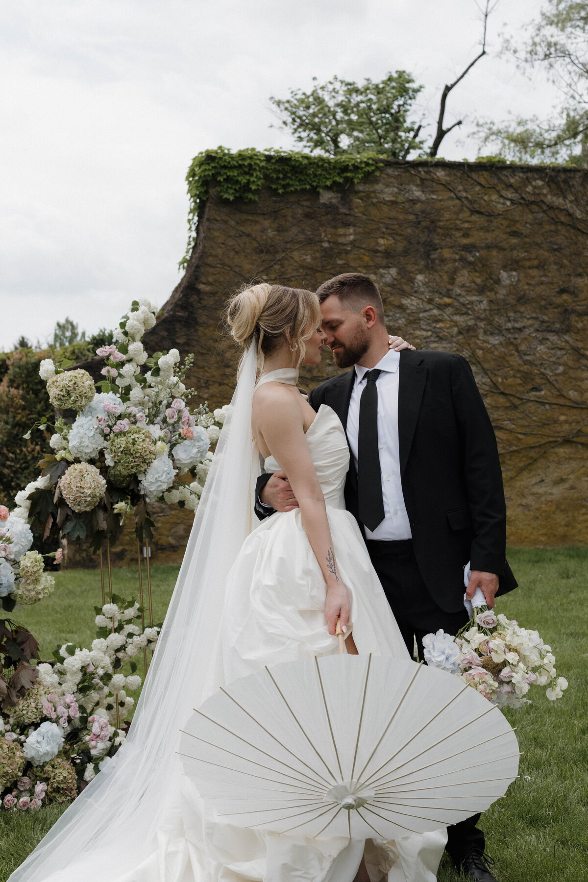 Documentary wedding photography capturing an intimate, romantic moment between bride and groom at a refined outdoor ceremony with floral details.