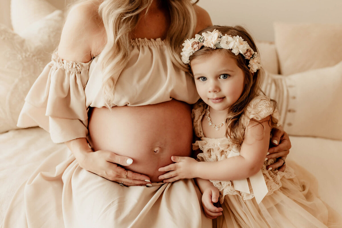 Little girl with a floral headband places her hand on her mother's pregnant belly, Edmond, Oklahoma.