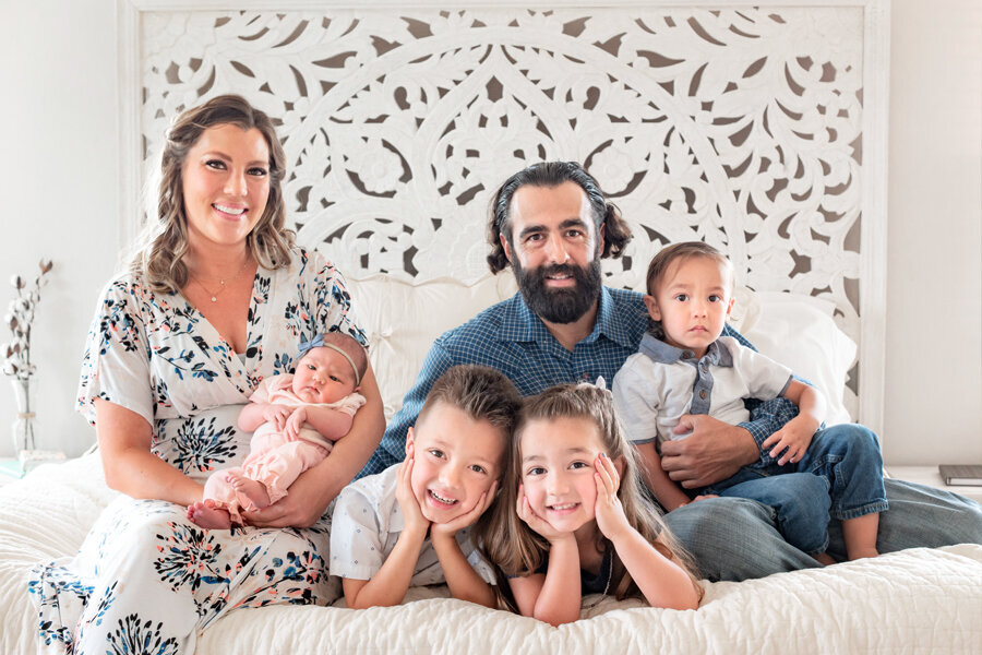 Family of 6 sitting on a white bed.