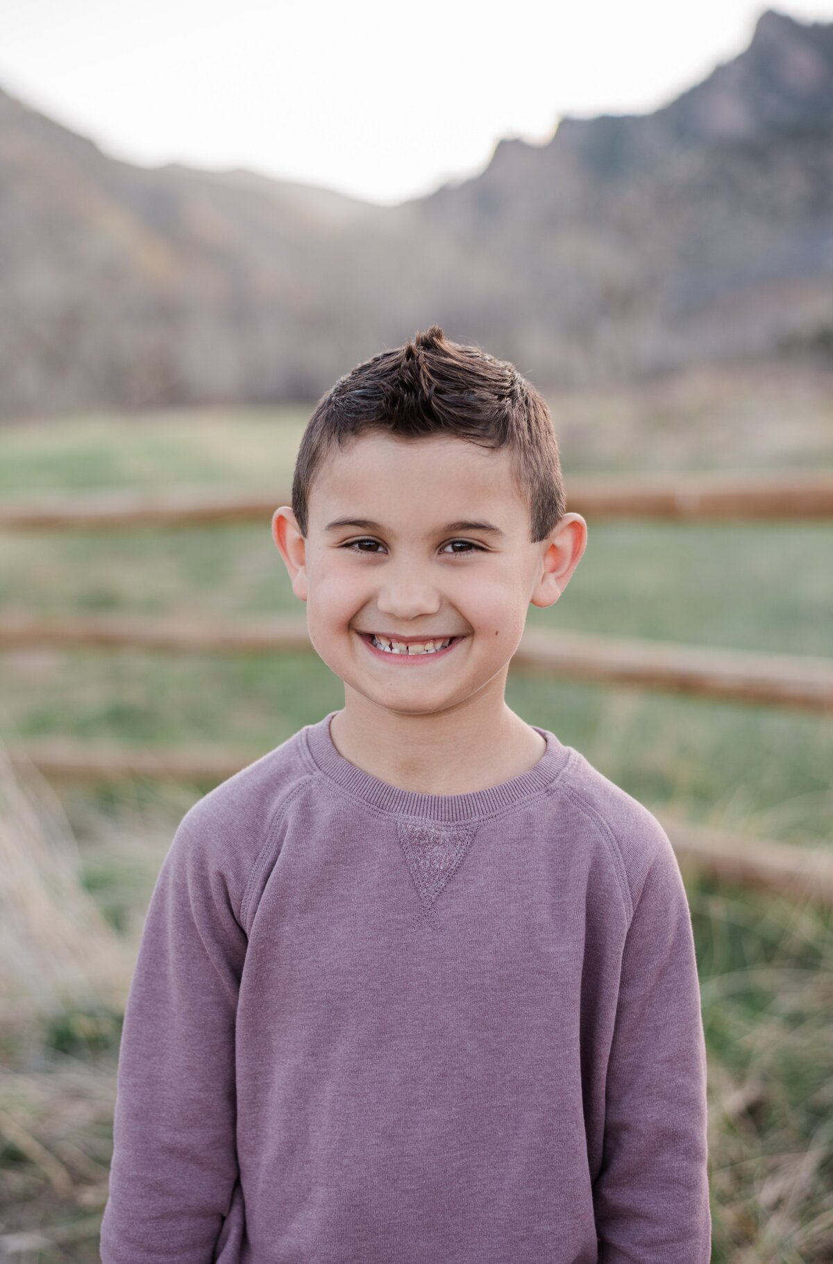 A young boy in a purple long sleeve sweater smiles at the camera with boulder flat irons behind him