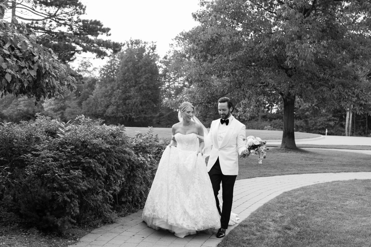 Black and white of bride and groom walking on a garden path