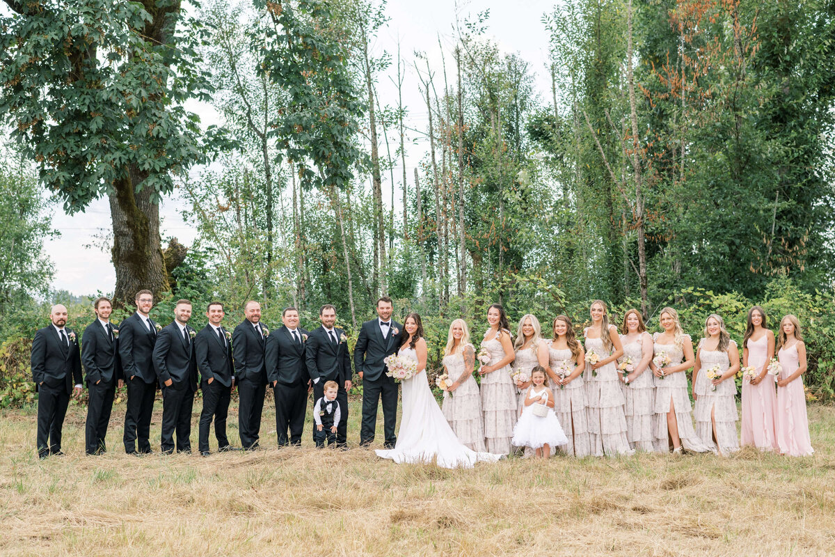 The members of a wedding party all stand outdoors and smile at the camera at a luxury wedding planned by Birdie June Events.