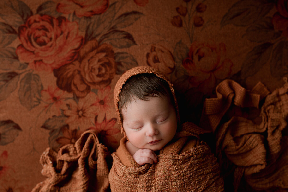Newborn swaddled in rust colored swaddle studio in swanton