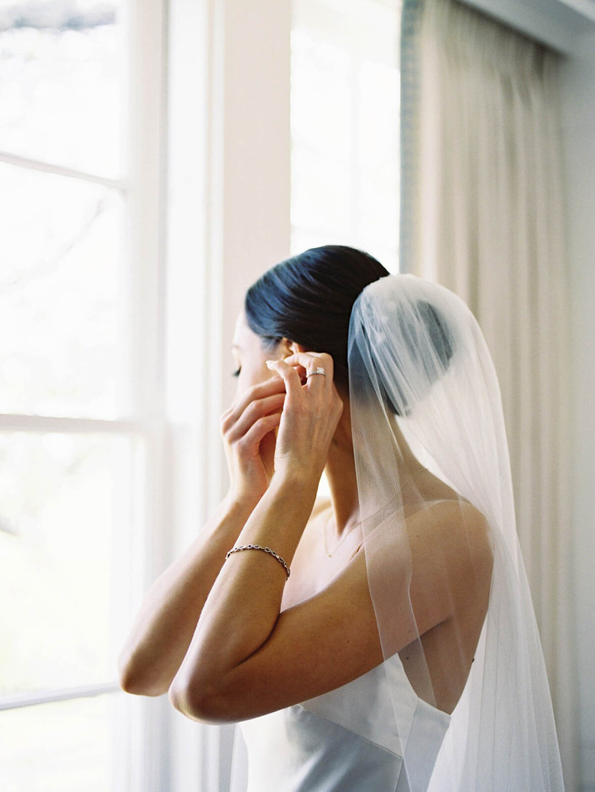 Bride puts earrings on by the window
