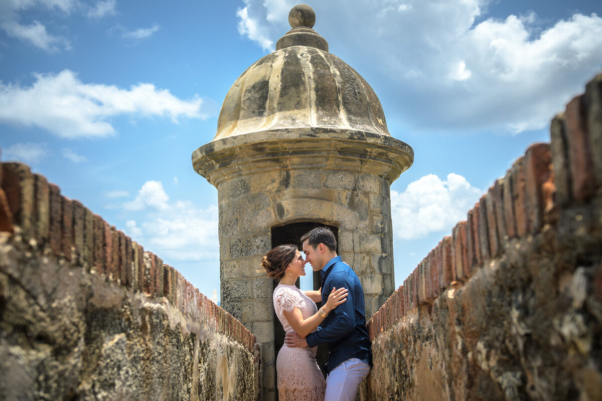 Romantic engagement portrait of a couple embracing by a historical stone tower, captured by Rodrigo Varela Photography in Miami, Florida. Timeless and intimate moment set against a unique architectural backdrop.