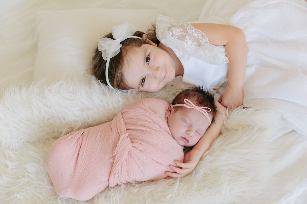 A small child laying next to a newborn on a bed