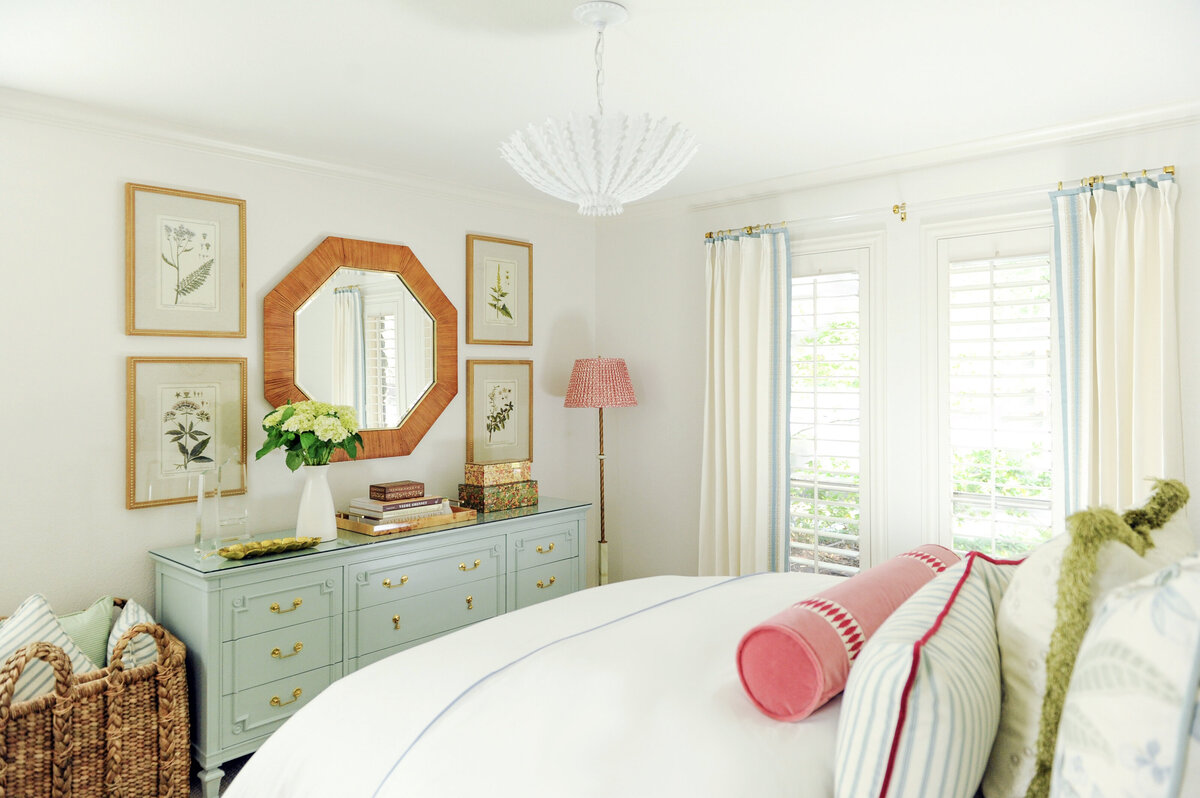 Interior Design Bedroom with Bed and Throw pillows, white chandelier, and dresser with mirror and art.