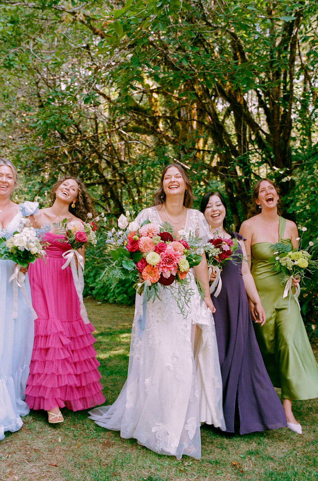 A bridal party stands outdoors smiling while holding their flower bouquets at vintage garden wedding.