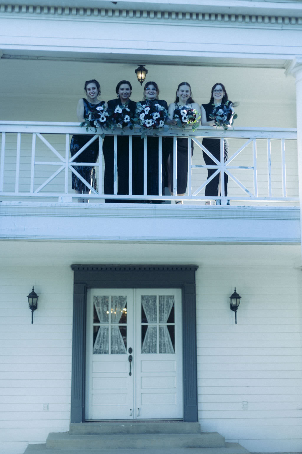 A wedding party smiling and looking down from a balcony.