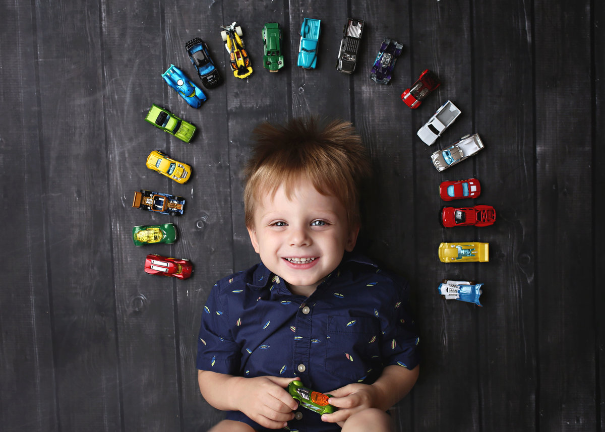 child laying on floor with arch of toy cars around his head