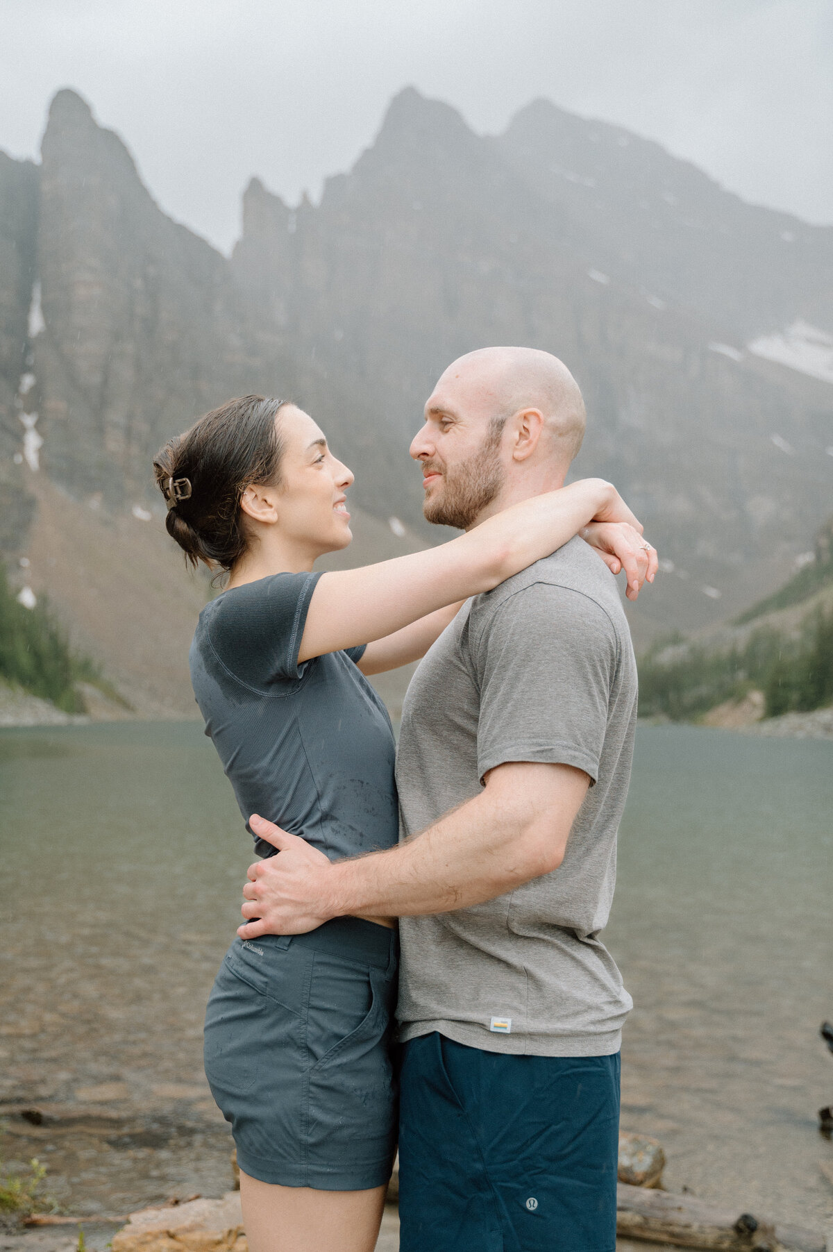 Couple embracing in front of Lake Agnes in the rain after getting proposed to. 