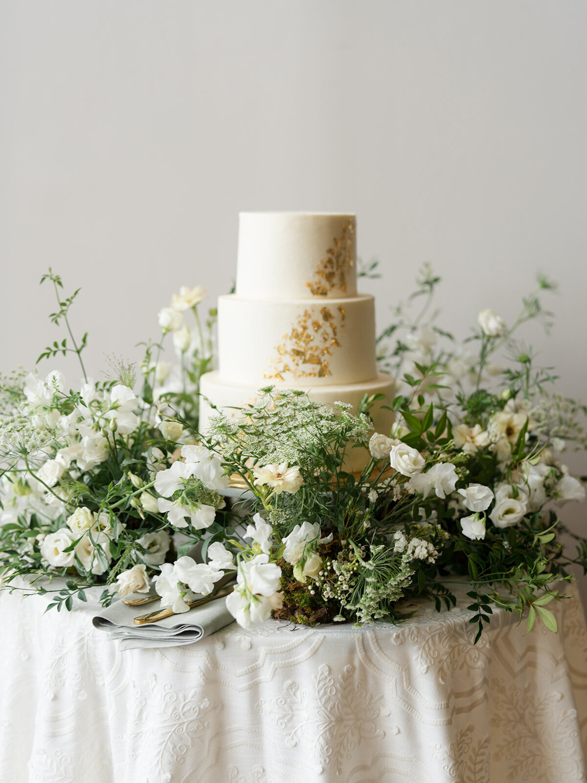 Lush green and white meadow-inspired flowers surrounding three tiered wedding cake
