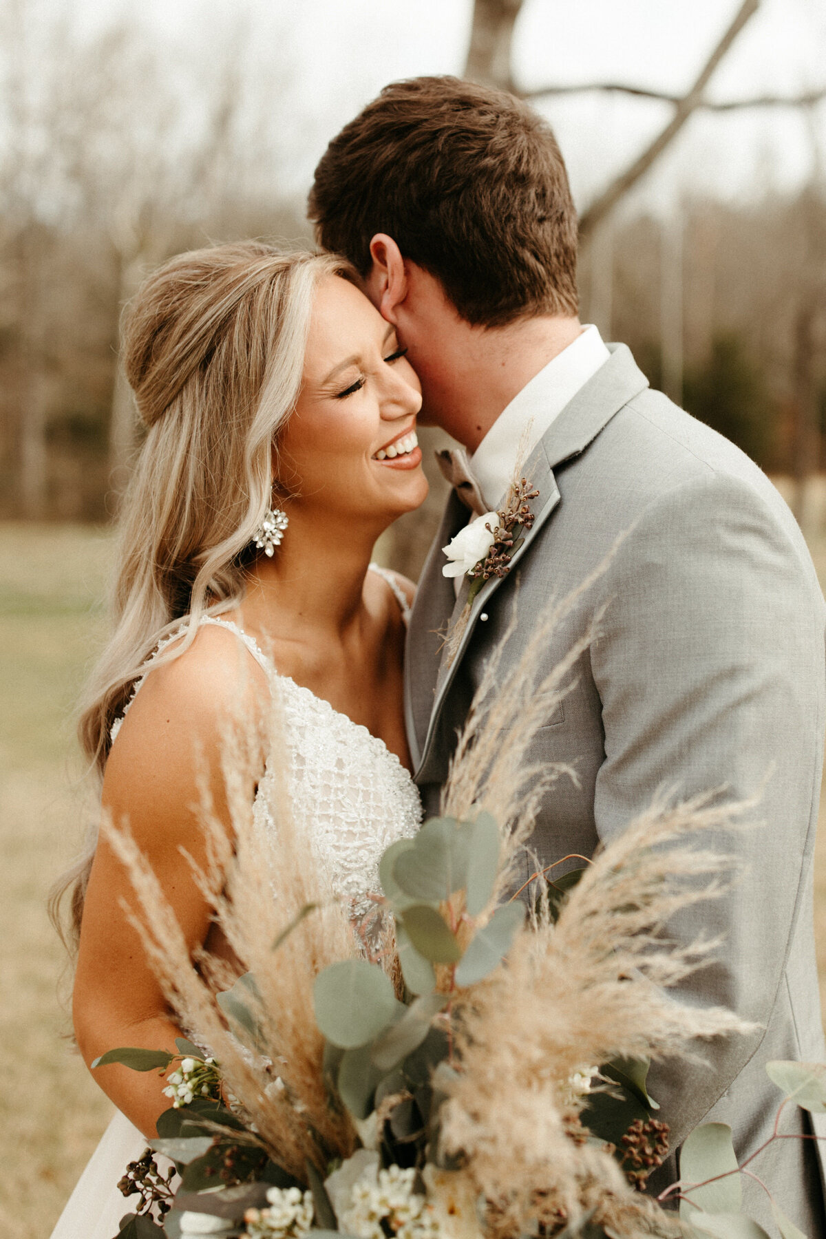 Bride with long loose curly hair laughing as her groom whispers in her ear