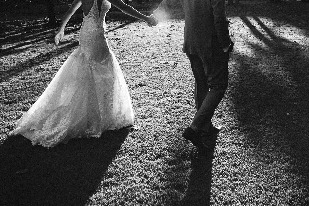 A couple walks hand-in-hand across a sunlit lawn at a private estate, captured in black and white by Mira Park Photography.