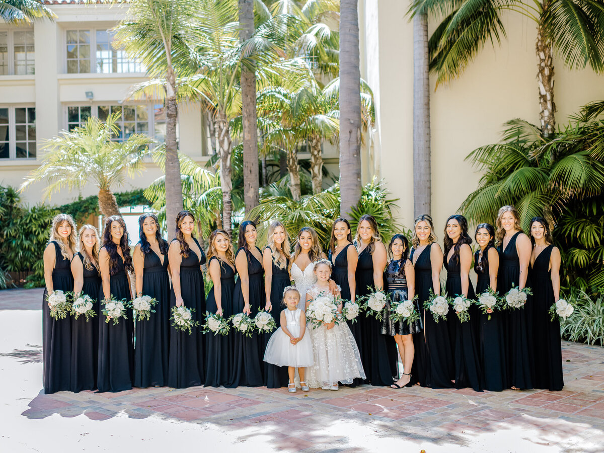 A stunning group shot of the bride with her bridesmaids in black dresses, posing together in the tropical courtyard at the Ritz-Carlton Laguna Niguel