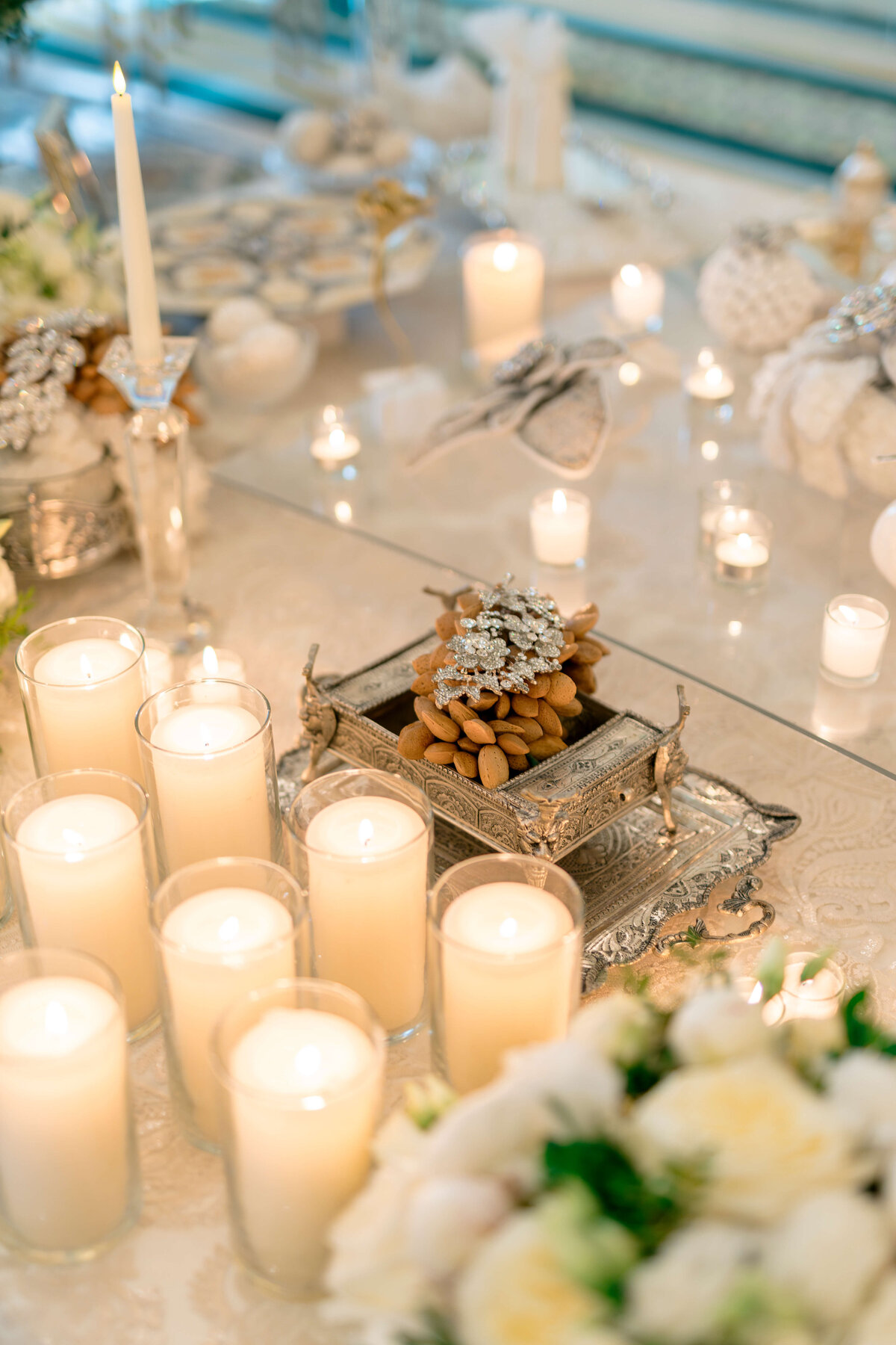 A beautifully arranged table with lit white candles, a decorative silver dish filled with almonds, and soft decorations. The ambiance is elegant and serene, with the focus on the warm candlelight and decorative details.