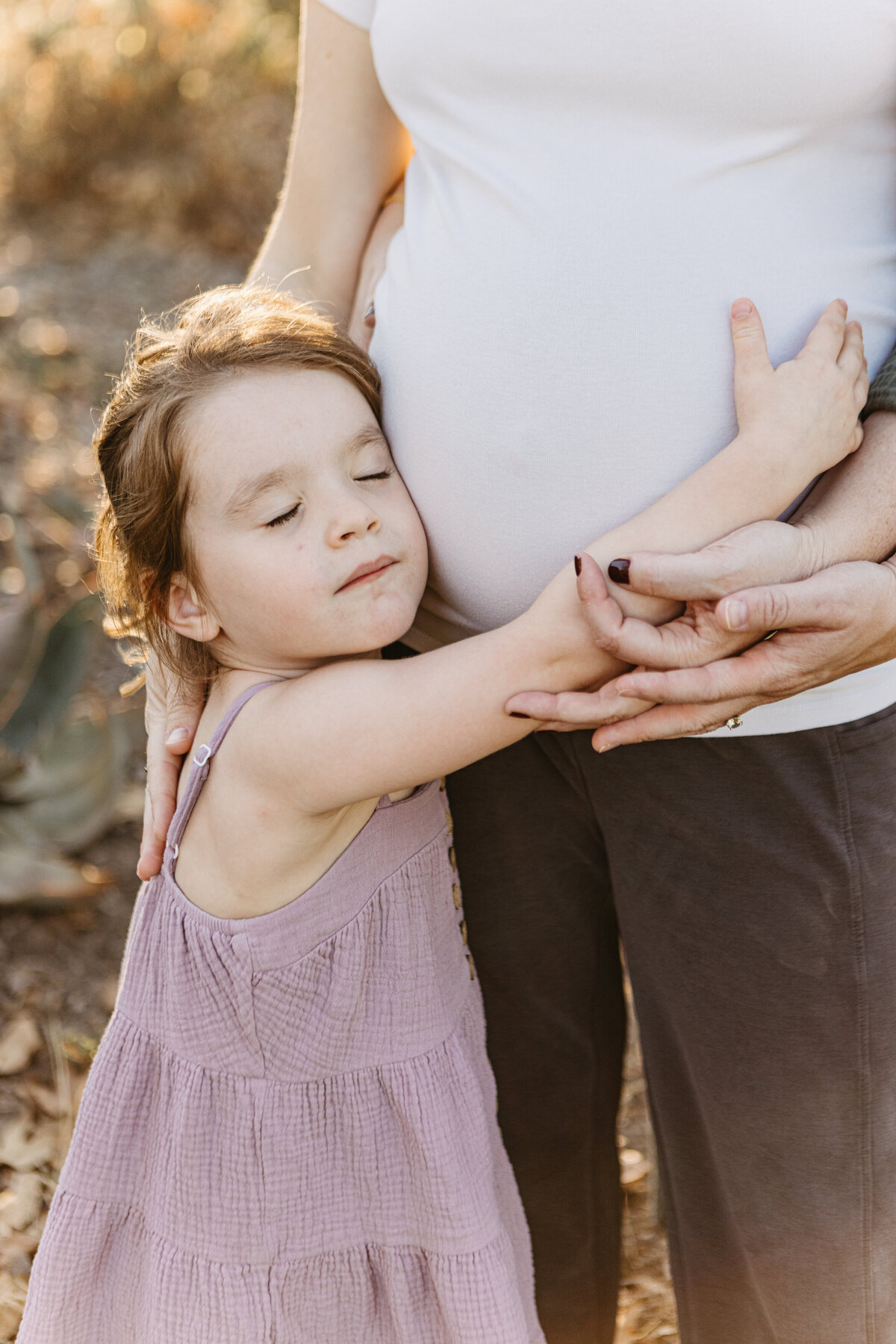 Little curls hugs her mom's maternity bump lovingly.