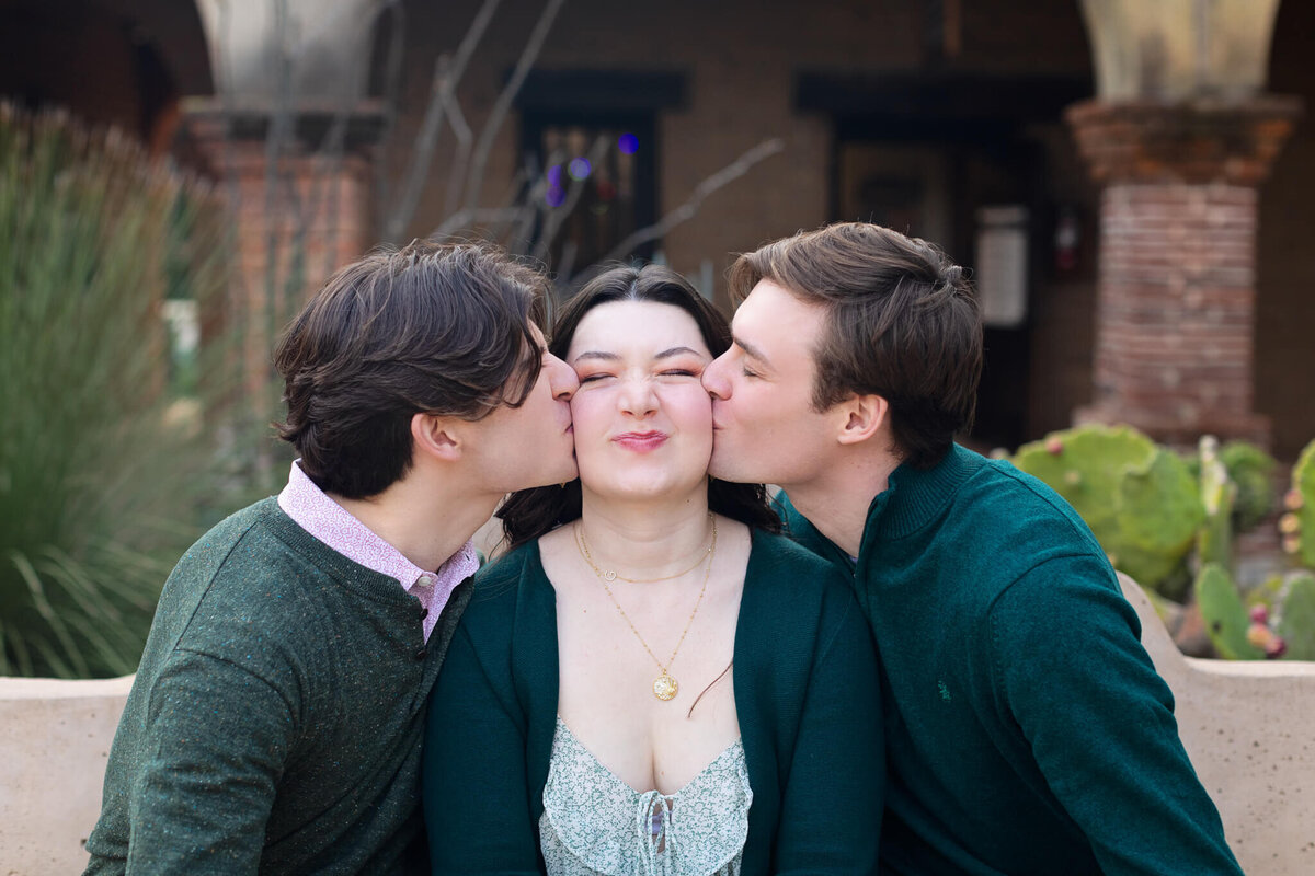 Two brothers kissing their sister's cheeks on either side of her while she is closing her eyes and making a funny face.