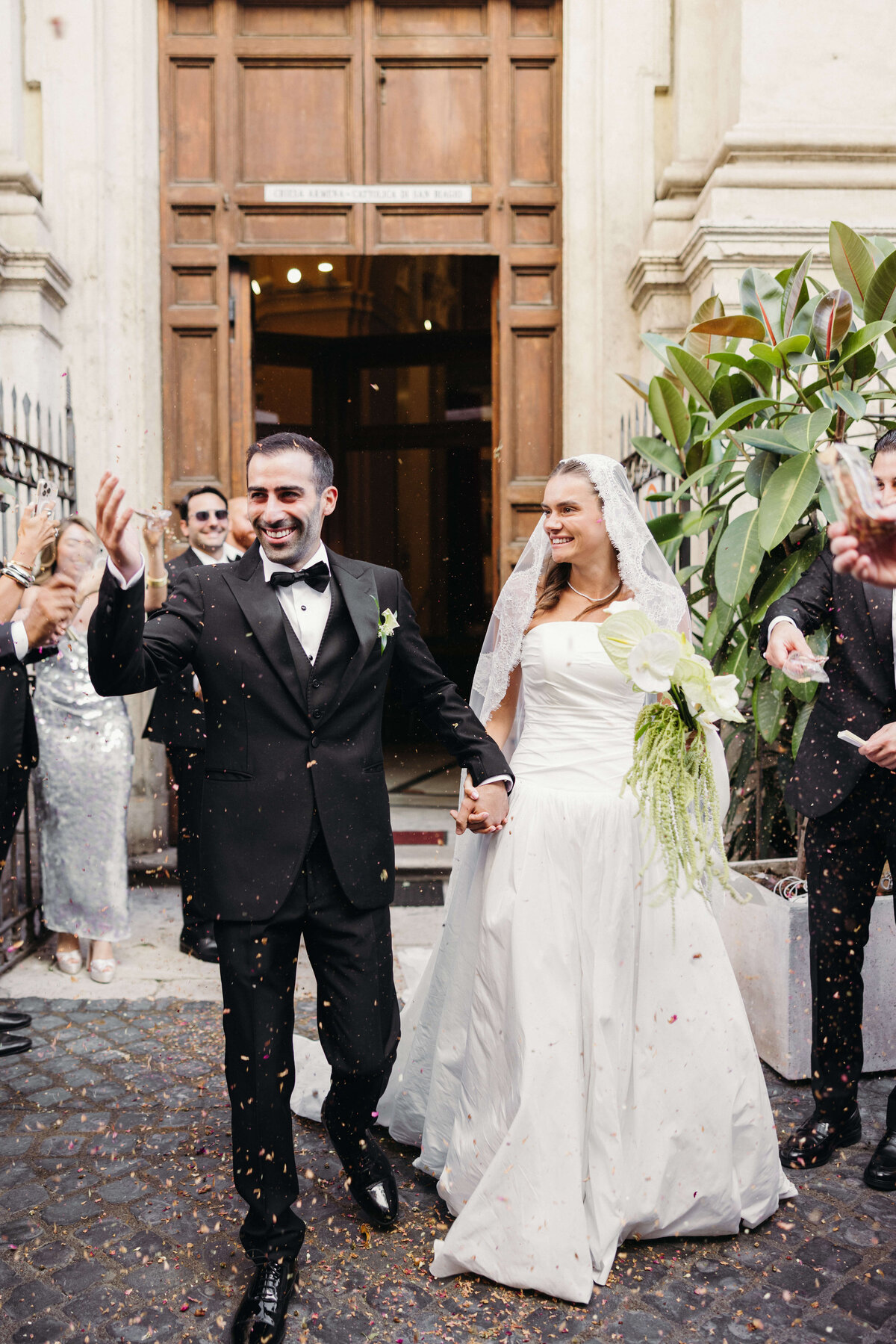 Bride and groom laughing as flower petals are tossed outside the church

