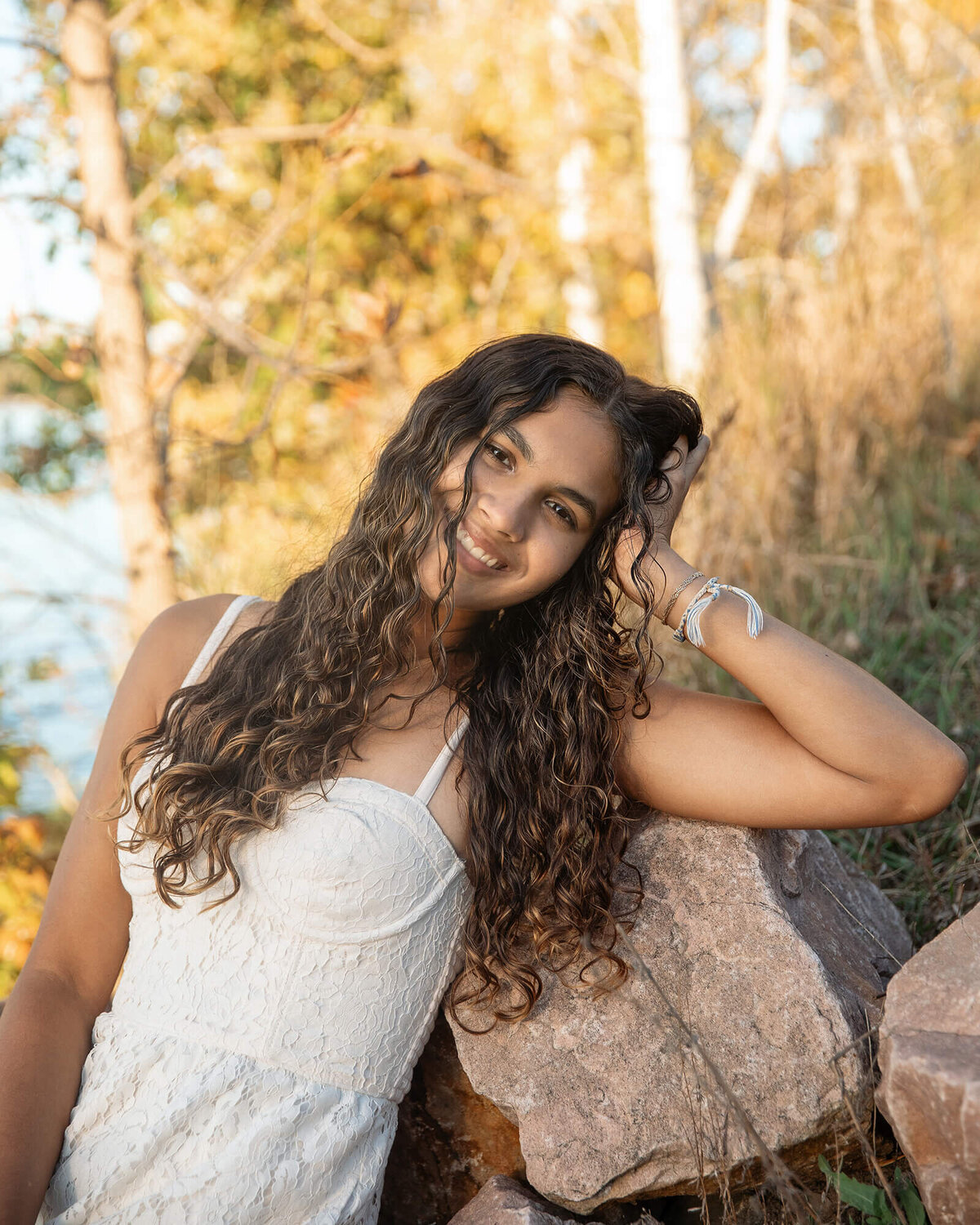 Senior girl in a white dress leaning on her arm smiling.
