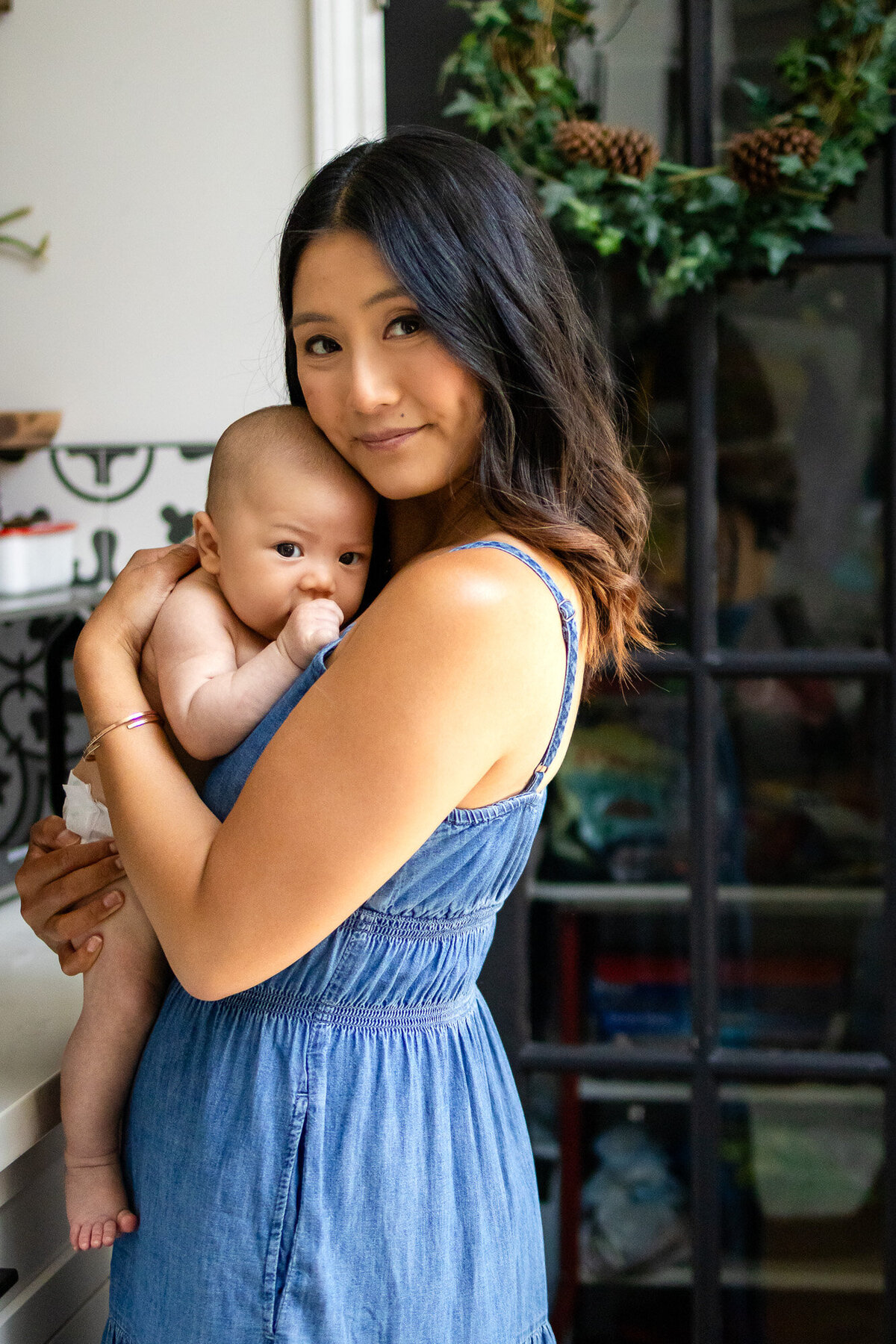 Mother holding baby on shoulder, standing by glass door, photographed by San Francisco newborn photographer.