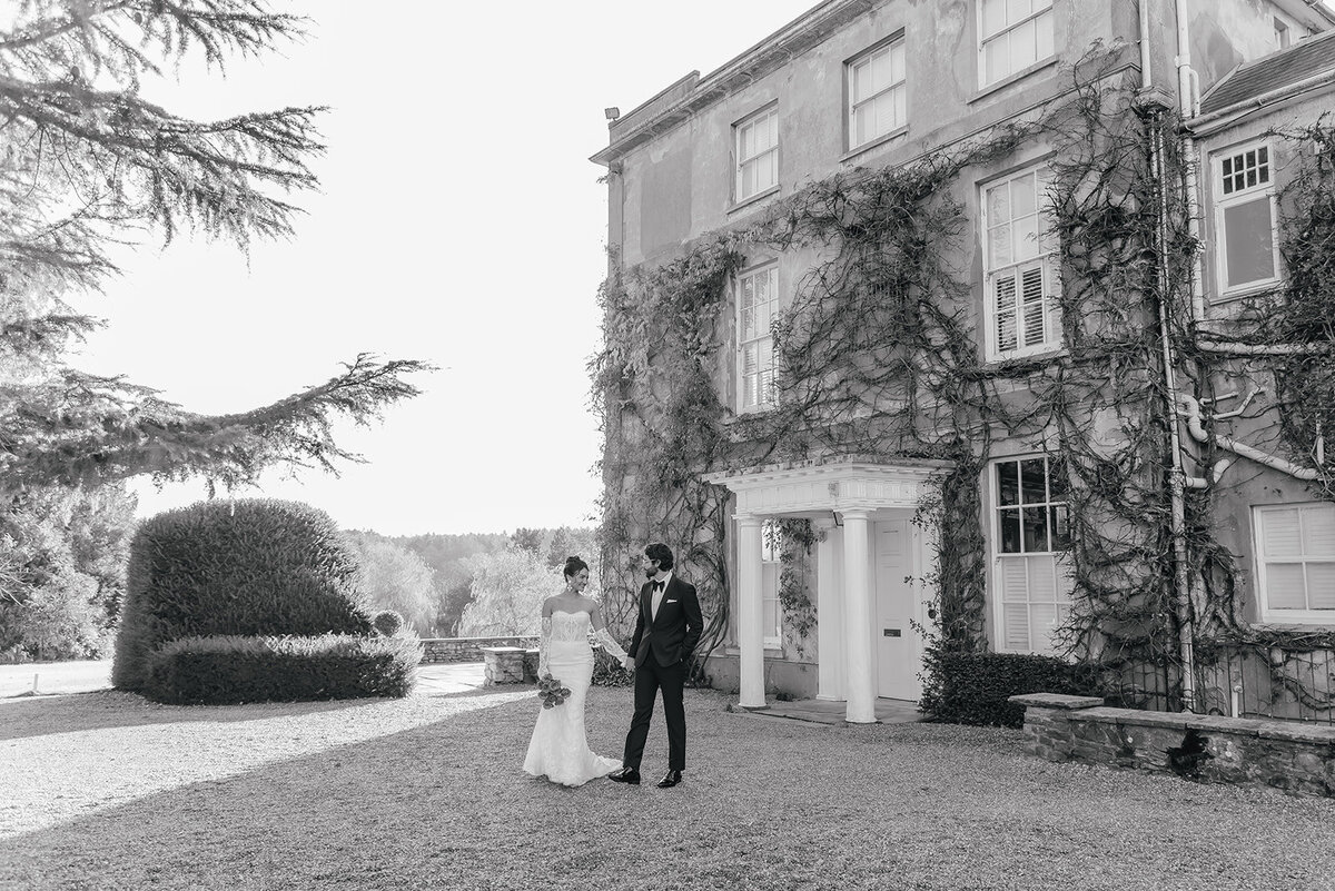 Bride in lace dress holding hands with her husband as they walk slowly down the pathway at Northbrook Park