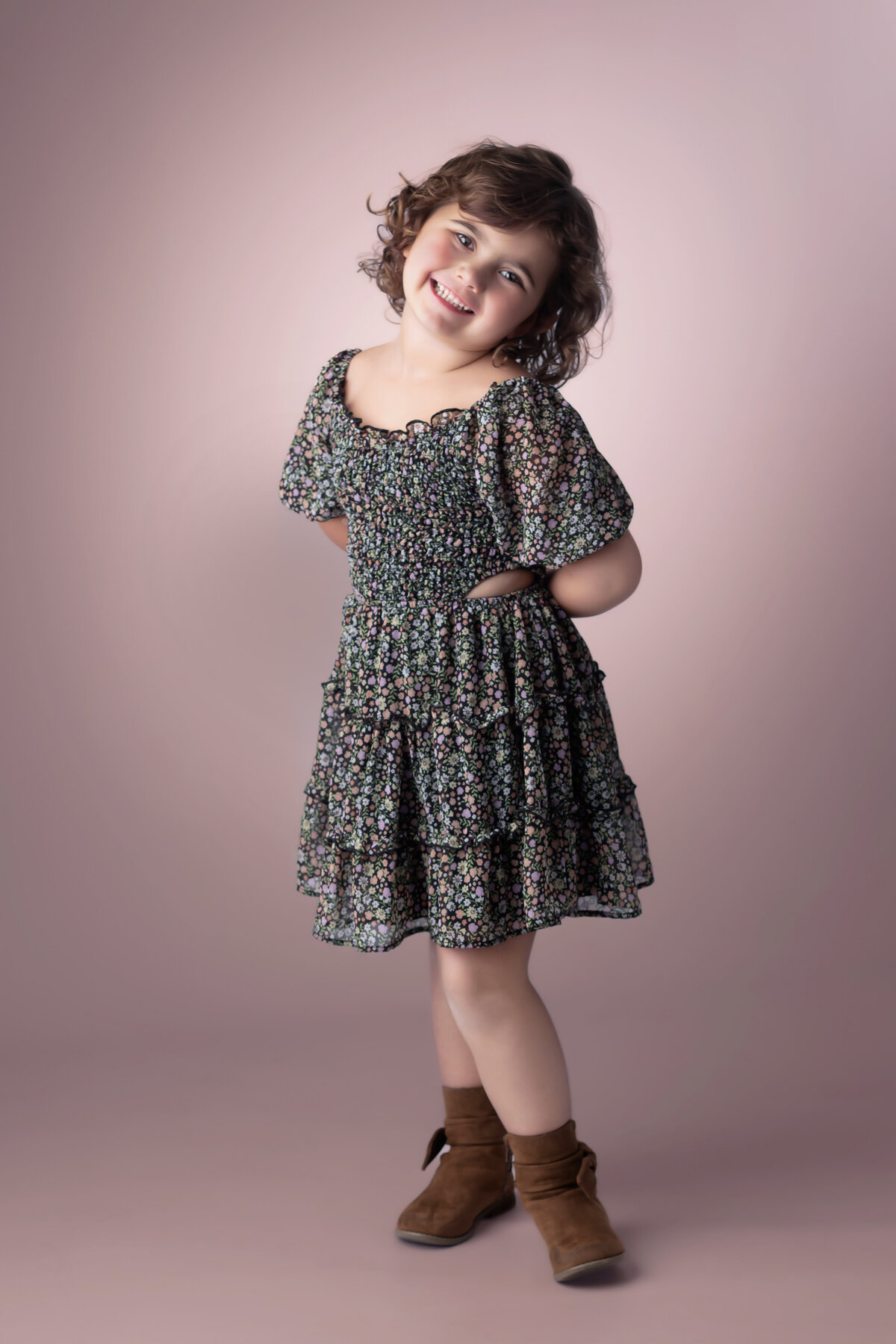 Girl stands in an Iowa Milestone Photography studio in a floral dress and a pink background