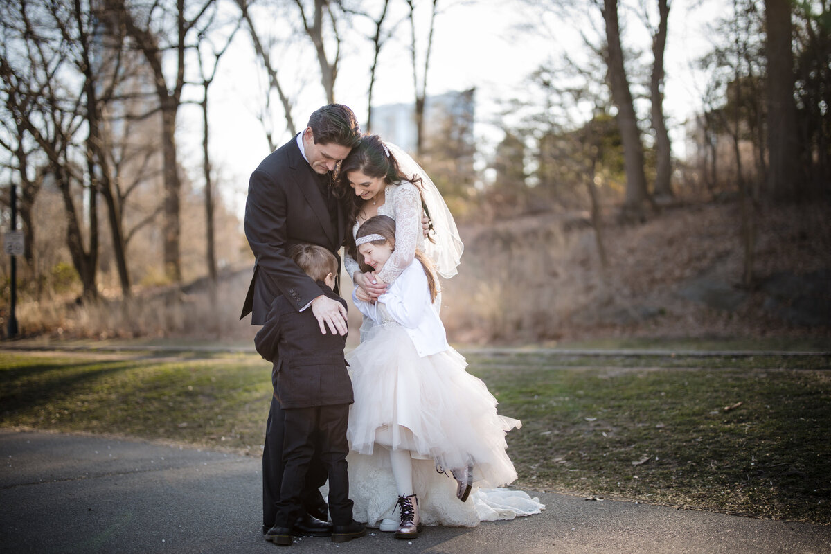 A bride and groom hugging two small kids together.