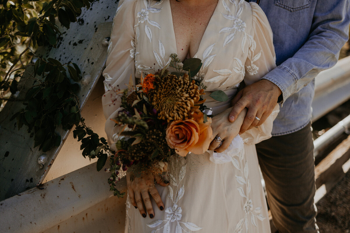 close up of newlyweds hands together holding the brides bouquet