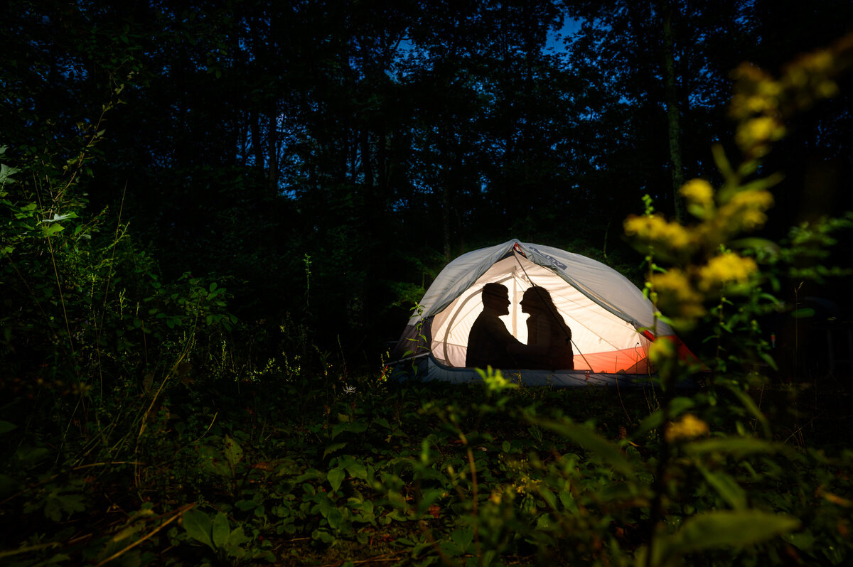 Silhouette of a couple sitting together inside of their tent in the woods