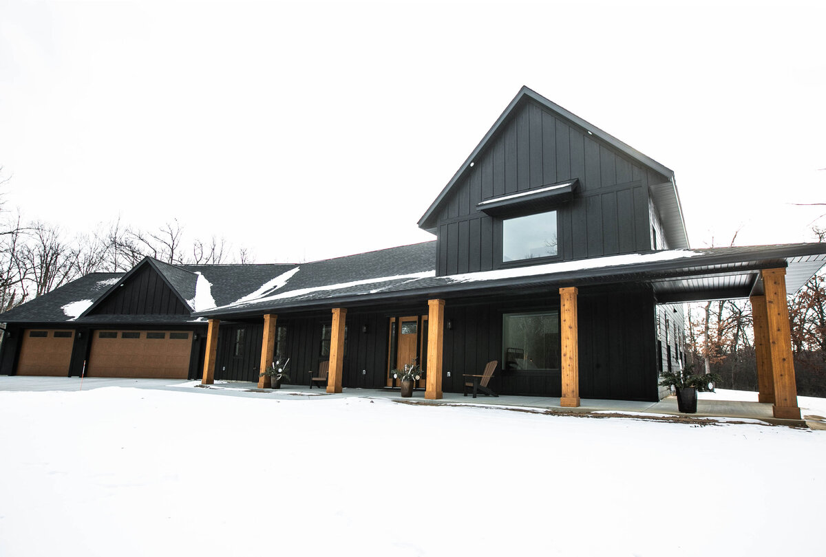 Exterior view of custom home in Elk River, Minnesota with black siding, wood details and front porch built by Cornerstone Custom Builds