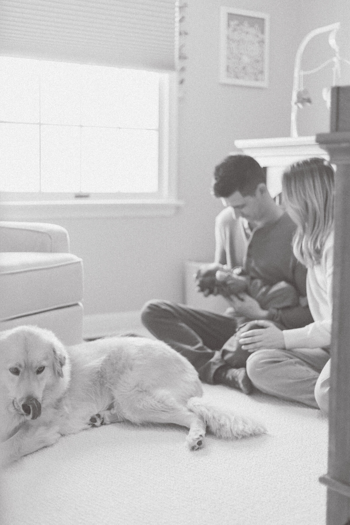New mom and dad holding baby in nursery with dog at their feet