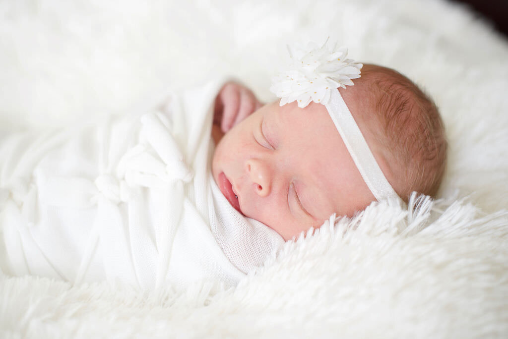 A newborn baby sleeping with a flower headband on.