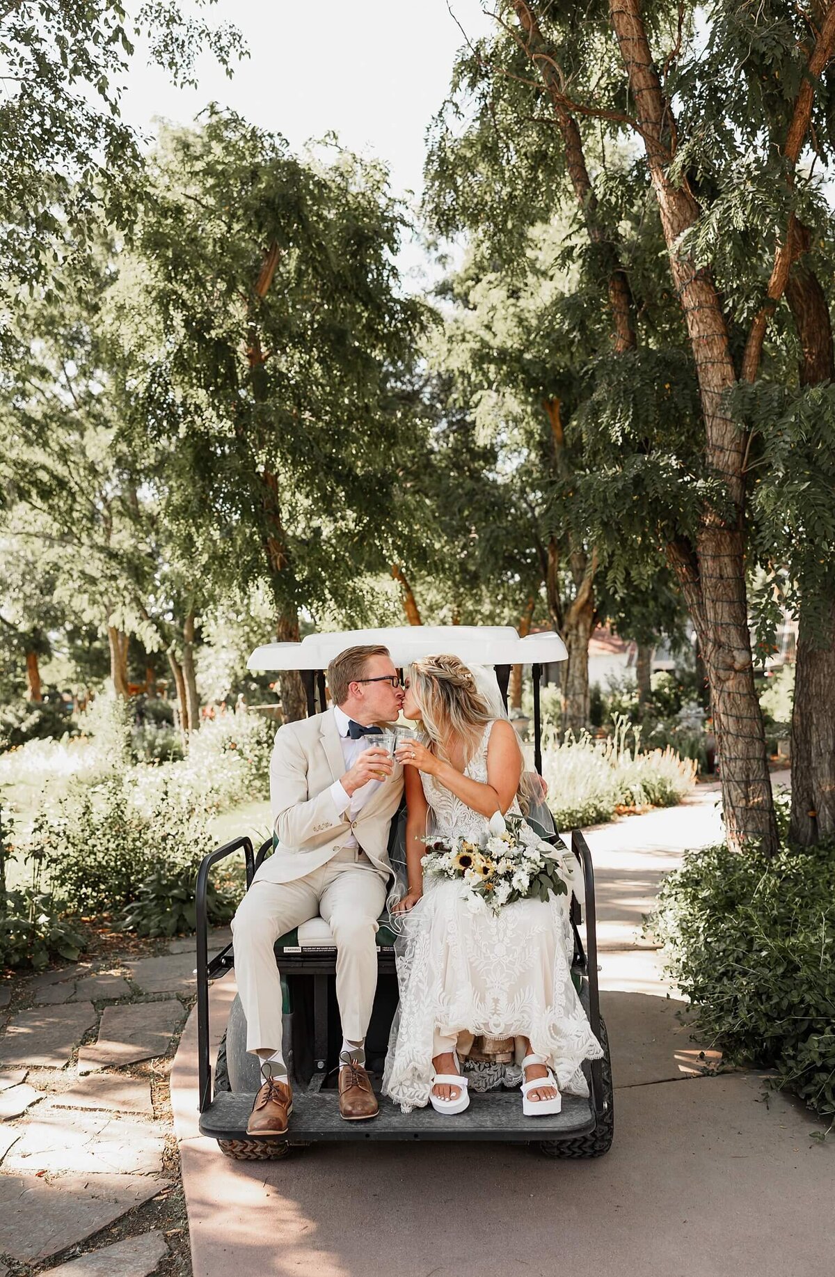 couple cheers their drink on a golf cart in tux and wedding dress