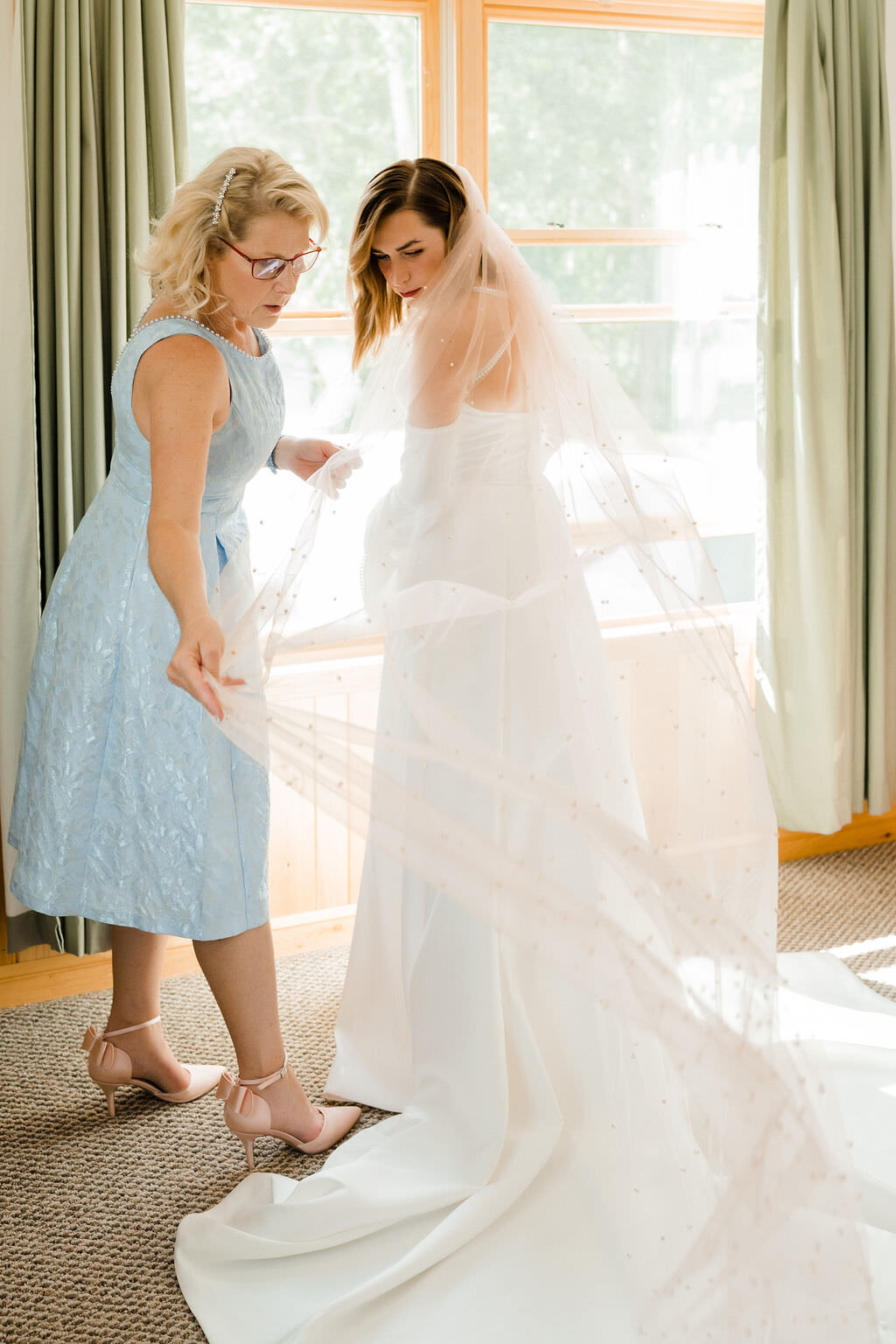 woman adjusting a brides veil as they both look back at it