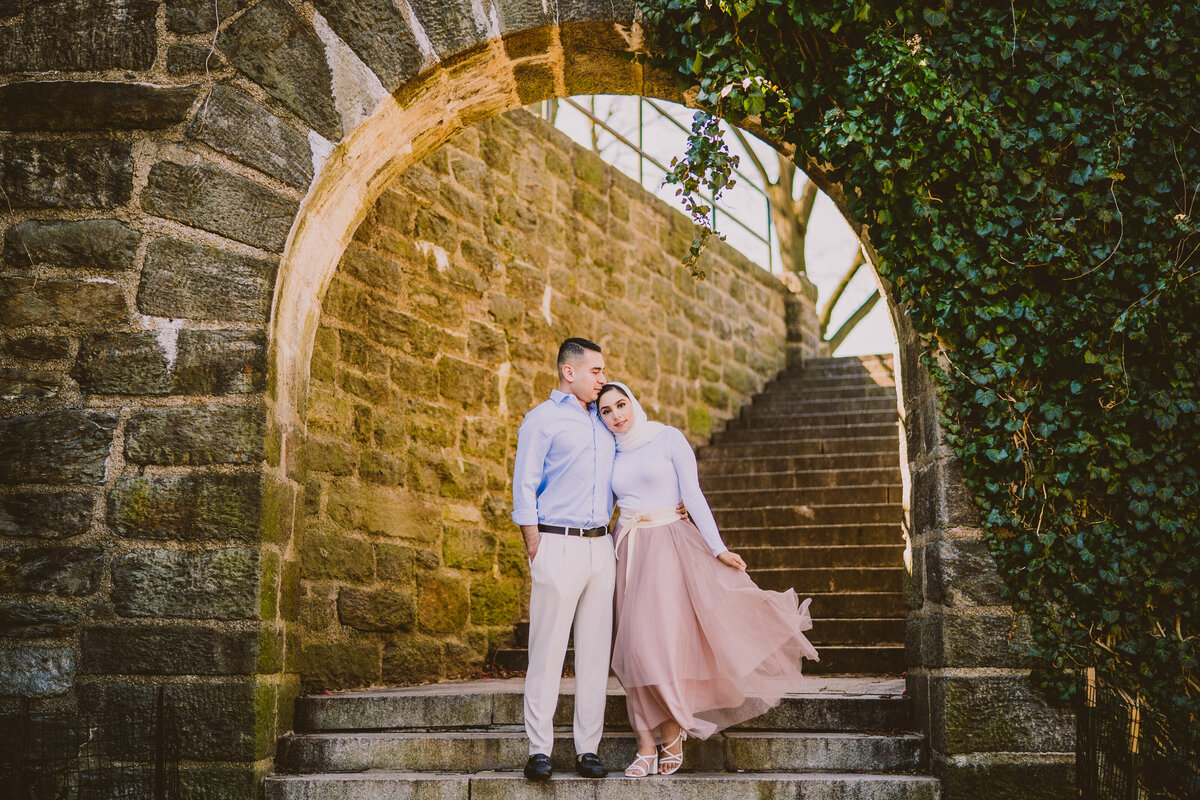 A pakistani muslim wedding couple standing on steps in front of an arch at fort tryon park in nyc