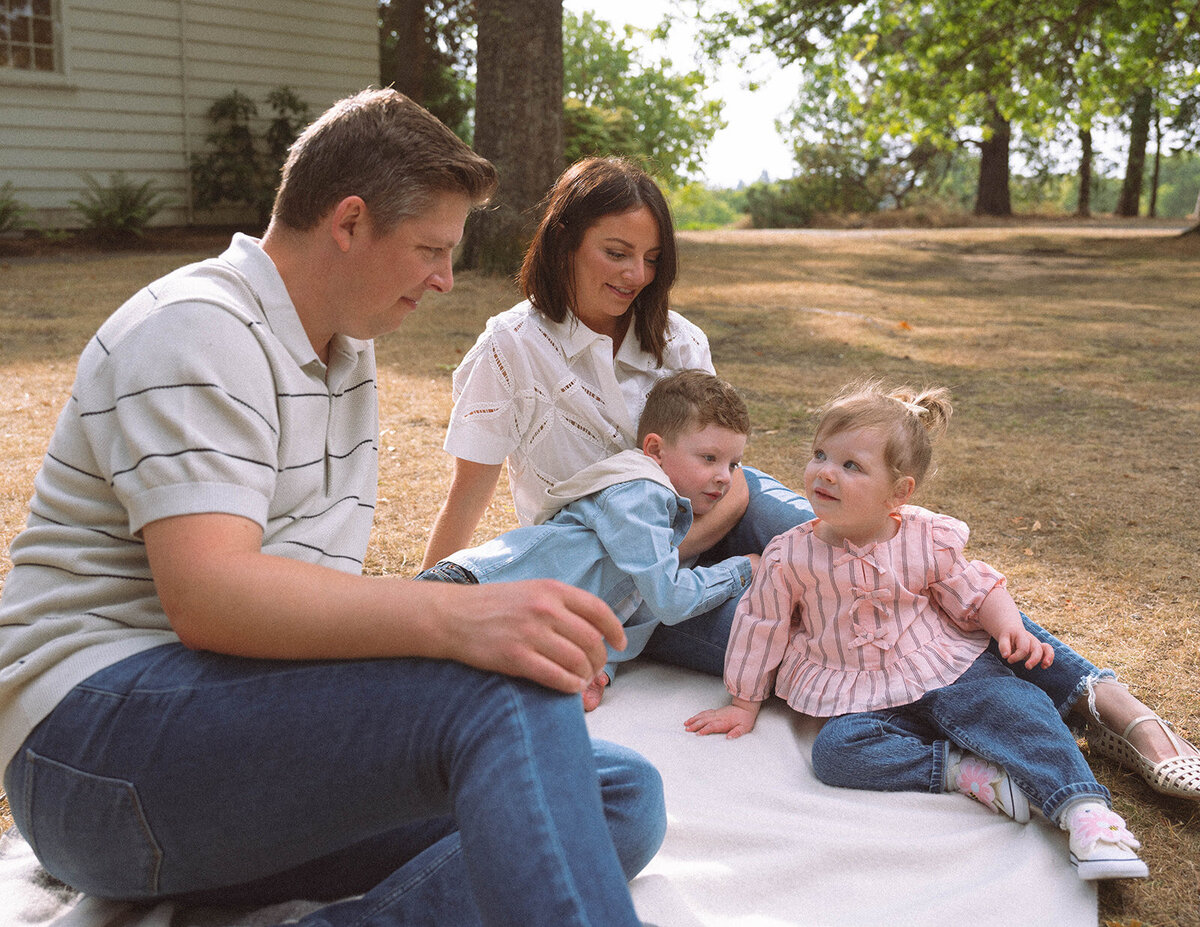 A family of four sits on a blanket under the trees, sharing an easy and relaxed moment during an Irvine family photo session.