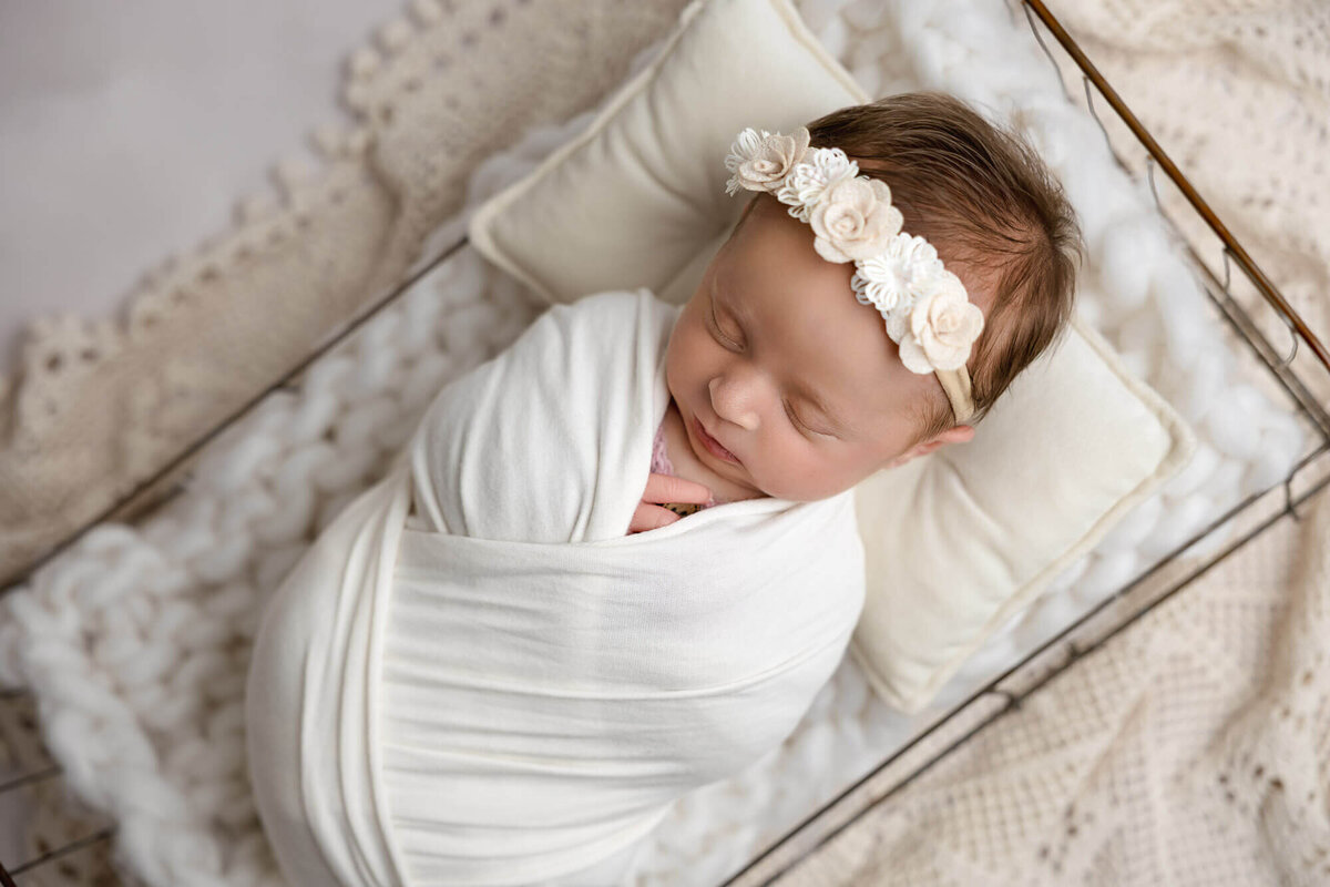 newborn girl swaddled in white with floral headband for photography session