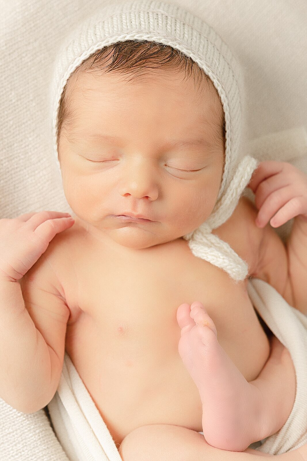 baby boy with white bonnet on and foot on chest