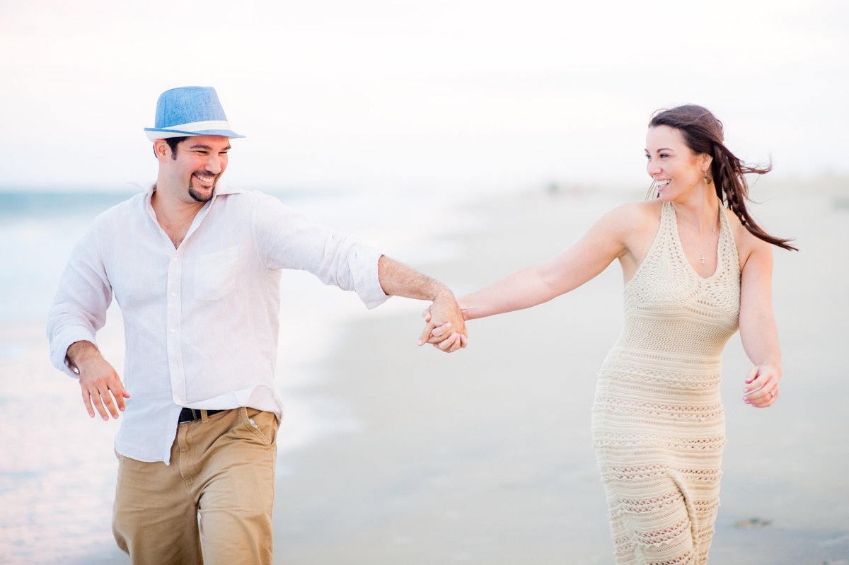 Couple running hand in hand on the beach smiling at each other.