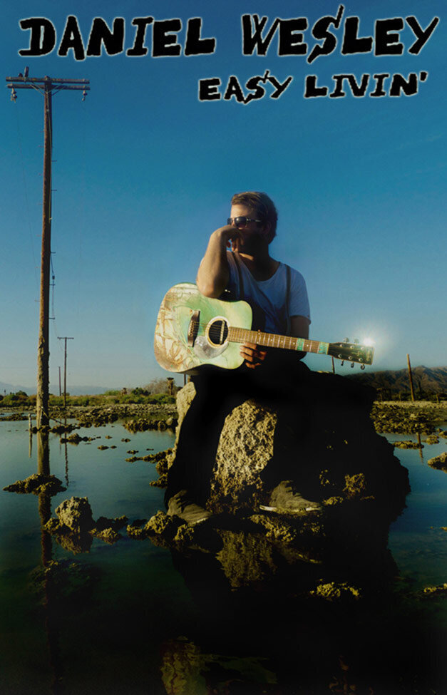 Poster Music Artist Daniel Wesley sitting on rock wearing sunglasses pools of water around him painted blue acoustic guitar in his lap